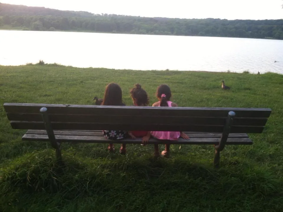 Three little girls on a bench by the lake.