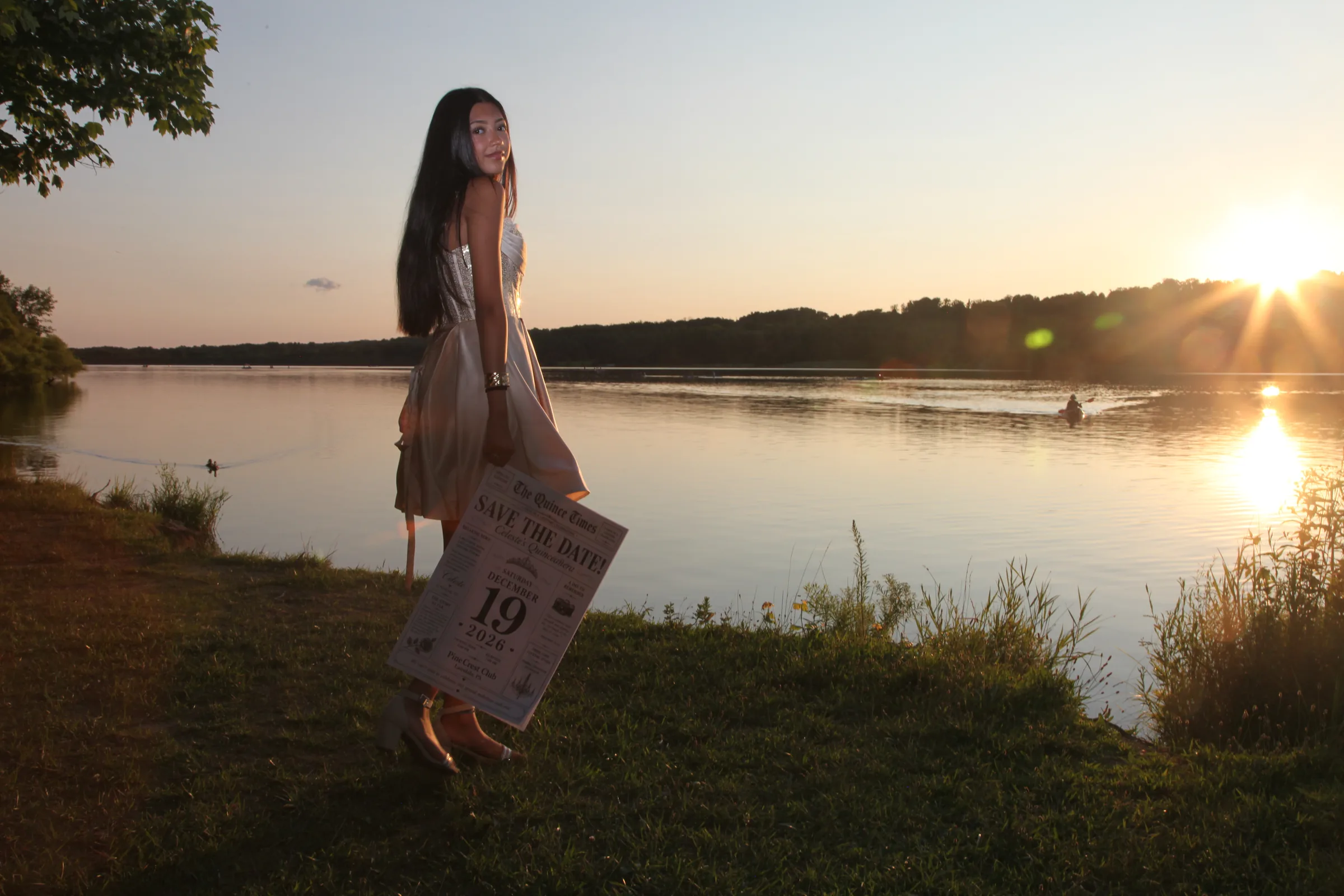 Celeste by the lake at sunset, holding the Save the Date newspaper.